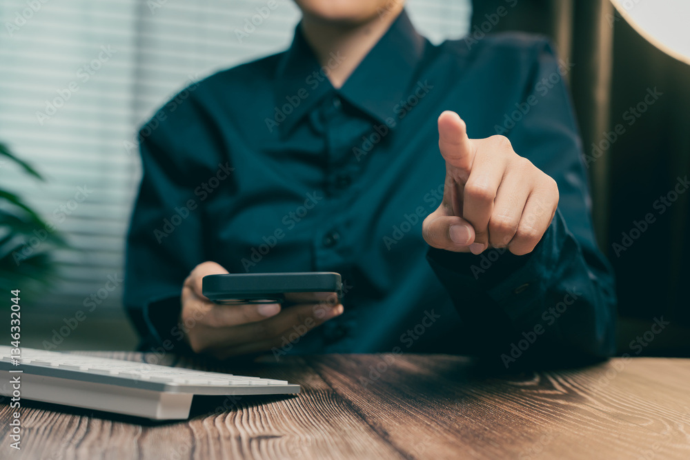 Poster person pointing while holding smartphone and sitting at a desk with a computer keyboard, business co