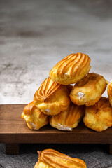 French eclair with custard. Profiteroles with cream on a white plate. Side view. Homemade pastries with cream. Grey background. Profiteroles with coffee.