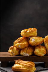 French eclair with custard. Profiteroles with cream on a white plate. Side view. Homemade pastries with cream. Dark background. Profiteroles with coffee.