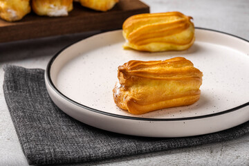 French eclair with custard. Profiteroles with cream on a white plate. Side view. Homemade pastries with cream.