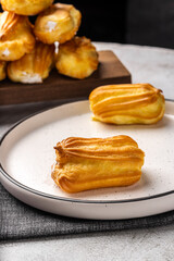 French eclair with custard. Profiteroles with cream on a white plate. Side view. Homemade pastries with cream.