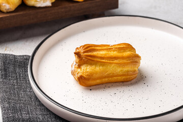 French eclair with custard. Profiteroles with cream on a white plate. Side view. Homemade pastries with cream.