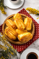 French eclair with custard. Profiteroles with cream on a wooden plate. Eclairs tow view. Flatlay. Natural lighting. Homemade pastries with cream.