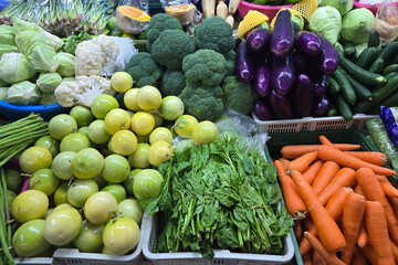 A vibrant display of assorted fresh vegetables and fruits including passion fruits, carrots, broccoli, spinach, and eggplants at a local wet market.