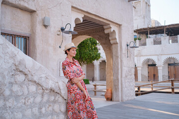 Young woman in an ethnic dress and hat exploring Al Seef Park in Dubai. Surrounded by traditional Emirati architecture and modern vibes, she enjoys the charm of Dubai Creek's cultural heritage.
