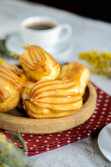 French eclair with custard. Profiteroles with cream on a wooden plate. Eclairs close up. Natural lighting. Homemade pastries with cream.
