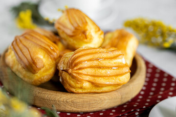 French eclair with custard. Profiteroles with cream on a wooden plate. Eclairs close up. Natural...