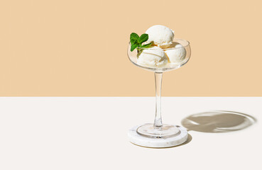 Scoops of vanilla ice cream in a tall glass on a beige white background. Summer refreshing dessert concept