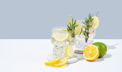 Two glasses fresh lemonade with lemon, lime, rosemary and ice. Citrus cocktail mojito on a white blue background.