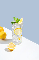 Lemonade with lemon, mint and ice in a glass on a white  blue background with shadow and fruits.