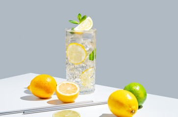 Lemonade with lemon, mint and ice in a glass on a white gray background with shadow and fruits. © Kufotos