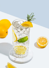 Mojito cocktail with  lemon, rosemary and ice in a glass on a white blue background with  fruits.