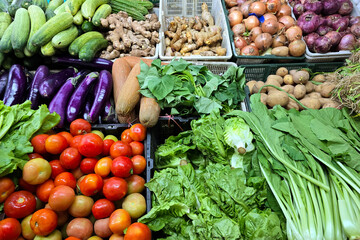 A vibrant display of fresh vegetables at a local market, featuring tomatoes, cucumbers, eggplants, leafy greens, potatoes, onions, and ginger.