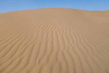 View of a high sand dune from bottom to top. Clear blue sky in the background. Shot in the desert, near the city of Yazd, Iran
