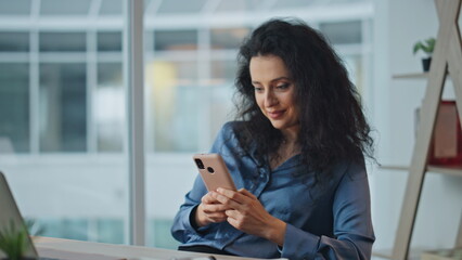 Relaxed employee using smartphone at desk. Smiling businesswoman messaging web
