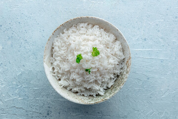White rice, cooked. A bowl of boiled long grain rice, a simple side dish, with fresh parsley leaves, shot from above