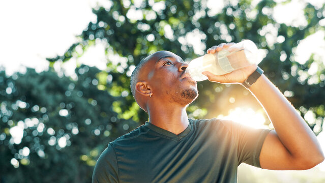Fitness, black man and drinking water outdoor for health, wellness and exercise recovery. Bottle, thirsty athlete and hydration at park for electrolytes, nutrition and detox in low angle on break - Powered by Adobe