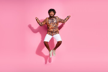 Young stylish man with curly hair jumps excitedly against a vibrant pink background, dressed in a...
