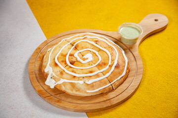 Malai Boti rounded flatbread stuffed naan served on a wooden plate with side dip on a white and yellow diagonal background Mediterranean food.