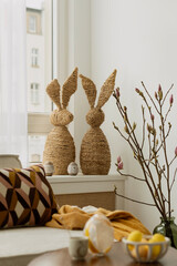 Minimalist Easter home decor with woven bunny figurines, soft textiles, and spring branches. A...