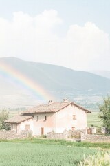 Beautiful countryside scene featuring a rustic farmhouse under a vibrant rainbow and majestic mountains, perfect for landscape and nature-themed projects.
