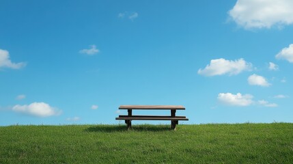 A wooden picnic table sits on a lush green hill under a blue sky. It can be used to portray relaxation, vacations, or outdoor recreation.
