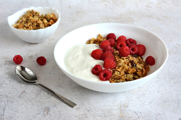 Delicious breakfast of granola with yogurt and fresh raspberries in a white bowl