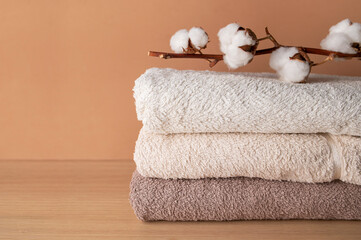 Stack of cotton towels and cotton branch with lush flowers on beige background. Natural bath...