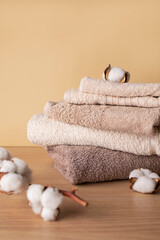 Stack of cotton towels and cotton branch with lush flowers on beige background. Natural bath...