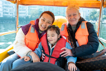 Pedal boat ride on the lake with a cute multiracial girl and her multiracial and multigenerational family. They are wearing red life jackets

