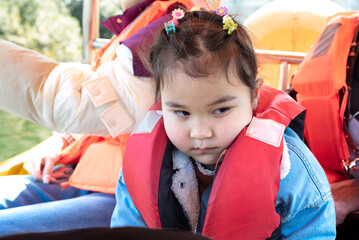 Little multiracial girl with red life jacket riding a pedal boat on a local lake. Weekend...