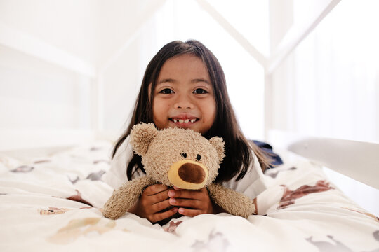 Happy young girl holding a teddy bear on the bed