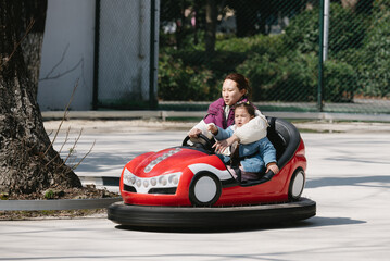 Happy and excited Chinese  woman and her cute little daughter driving bumper car in the amusement park. Happy people concept.
