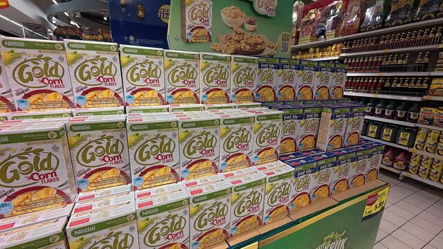 Commercially packaged cornflakes are displayed for sale in a large supermarket. They are organized by various brands and sizes, ensuring neat categorization for shoppers.