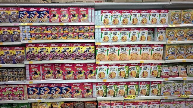 Commercially packaged cornflakes are displayed for sale in a large supermarket. They are organized by various brands and sizes, ensuring neat categorization for shoppers.