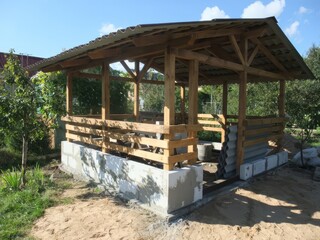 Completed wooden gazebo with a metal roof in a lush garden setting, offering shade and relaxation in a natural outdoor space