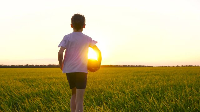 boy run across green meadow, holding rugby ball in hand. child races forward across grass, illuminated by first rays of sun. sense freedom, spirit adventure fill dynamic moment.