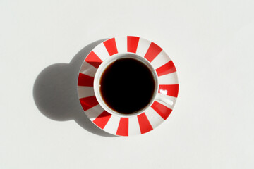 Top view on white and red stripes porcelain cup with espresso coffee with vivid shadows. Concept of...