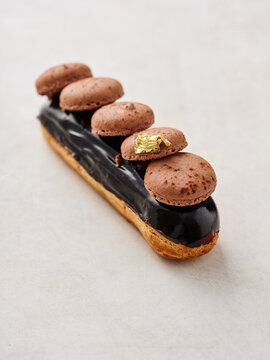 A beautifully crafted chocolate eclair is showcased with a glossy dark chocolate glaze. Delicate macarons sit atop, adding a gourmet touch