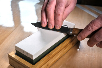 A close-up of a person sharpening a knife on a whetstone. The hands guide the blade at the correct angle, ensuring a precise and sharp edge.