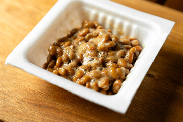 ネバネバの糸を引いている白いパック入りの納豆　木製テーブルの背景