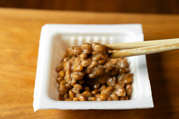 箸でかき混ぜてネバネバの糸を引いている納豆　白いパック　木製テーブルの背景