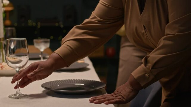 Close up on hands of Black female dinner host placing empty plate on dining table setting up festive dinner together with family members at home