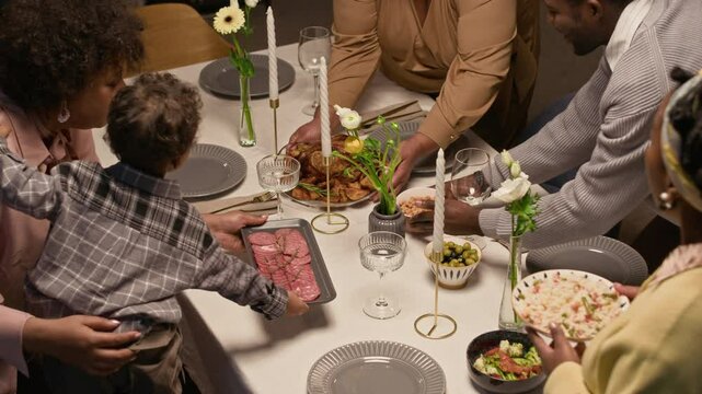 Happy Black senior woman raising toast with family members at festive home gathering then clinking glasses with playful little grandson sipping juice at dining table