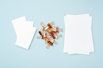 Heap of gold binder clips and memo note paper on light blue background