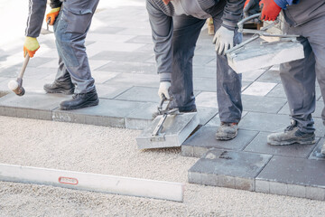 Construction workers laying pavement tiles using specialized tools and a rubber mallet for precise alignment. The process ensures stability in urban roadwork and landscaping projects.