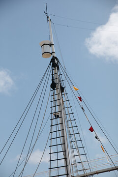 A ship's mast with signal flags at the top and lines of ropes.