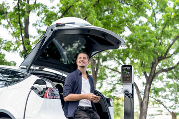 Man using smartphone online banking application to pay for electric car battery charging from EV...