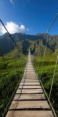 Obraz premium A breathtaking view of a long suspension bridge stretching across lush green hills, leading towards majestic mountains under a clear blue sky.