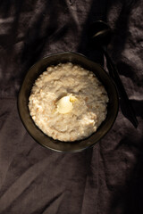 Oatmeal porridge with a piece of butter on a black background